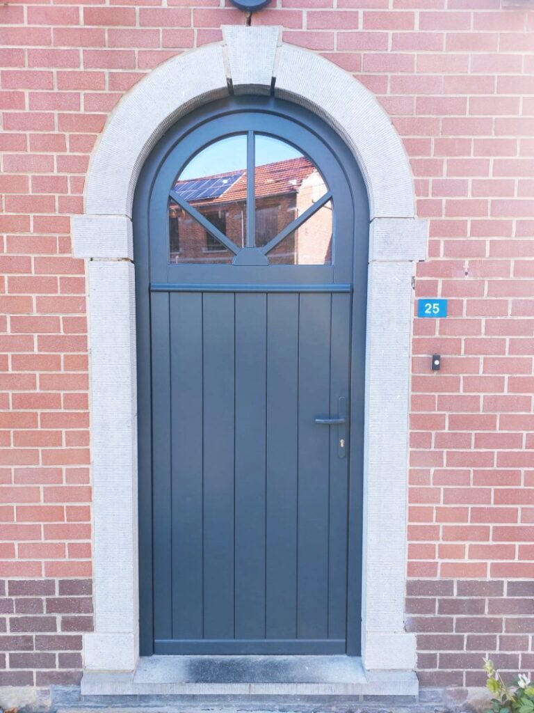 Porte d'entrée cintrée gris anthracite à lames verticales avec imposte vitrée en éventail sur façade en briques rouges