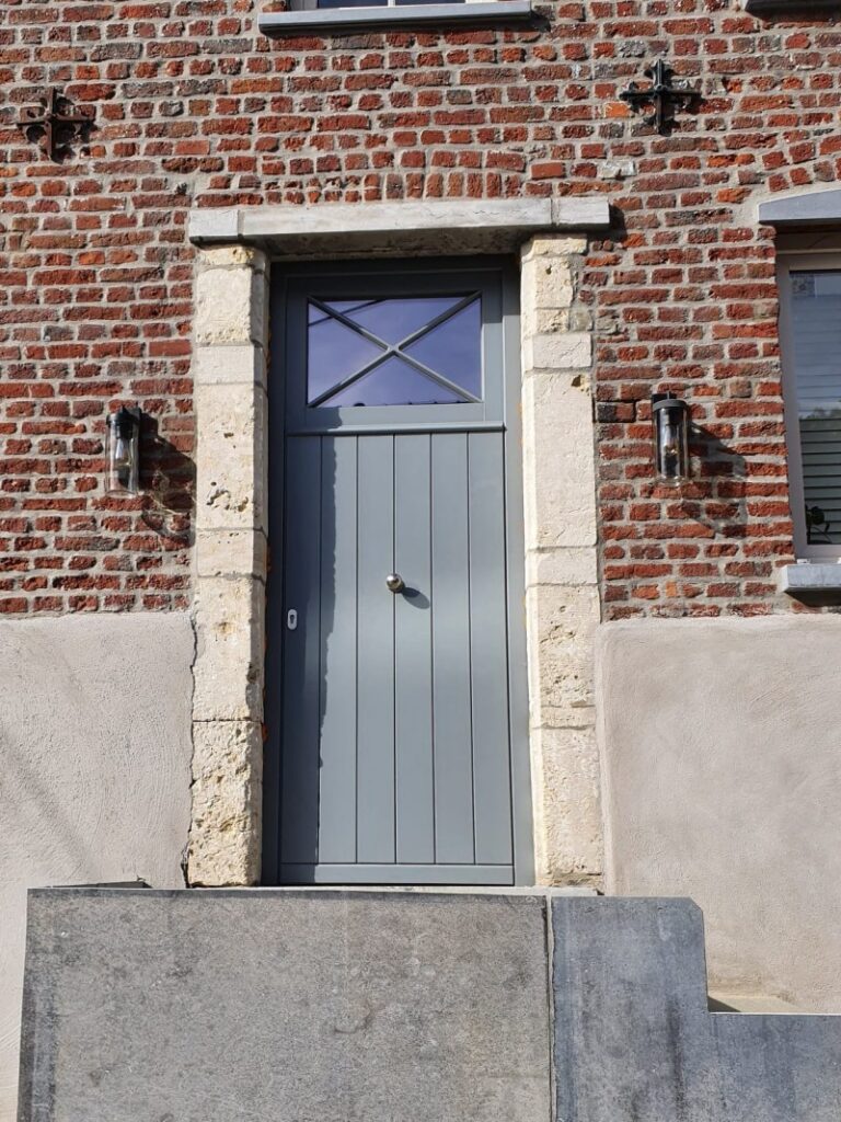 Porte d'entrée gris clair à lames verticales avec imposte vitrée à croisillon en X et bouton de tirage inox