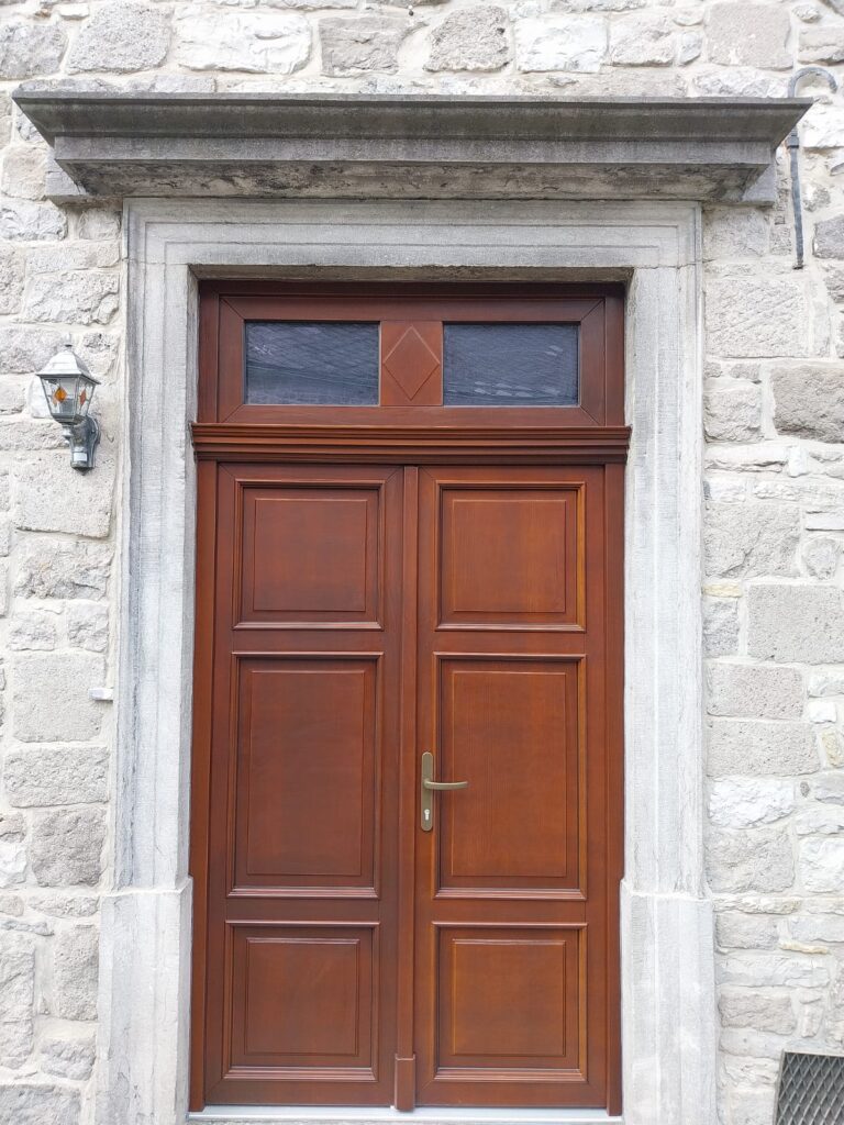 Double porte d'entrée en bois ton acajou à panneaux moulurés avec imposte vitrée à losange, dans un encadrement en pierre