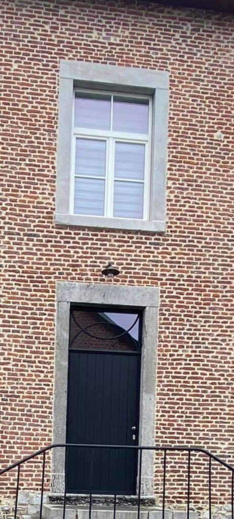 Porte d'entrée noire en bois à lames verticales avec imposte vitrée en ferronnerie, intégrée à une façade en briques anciennes